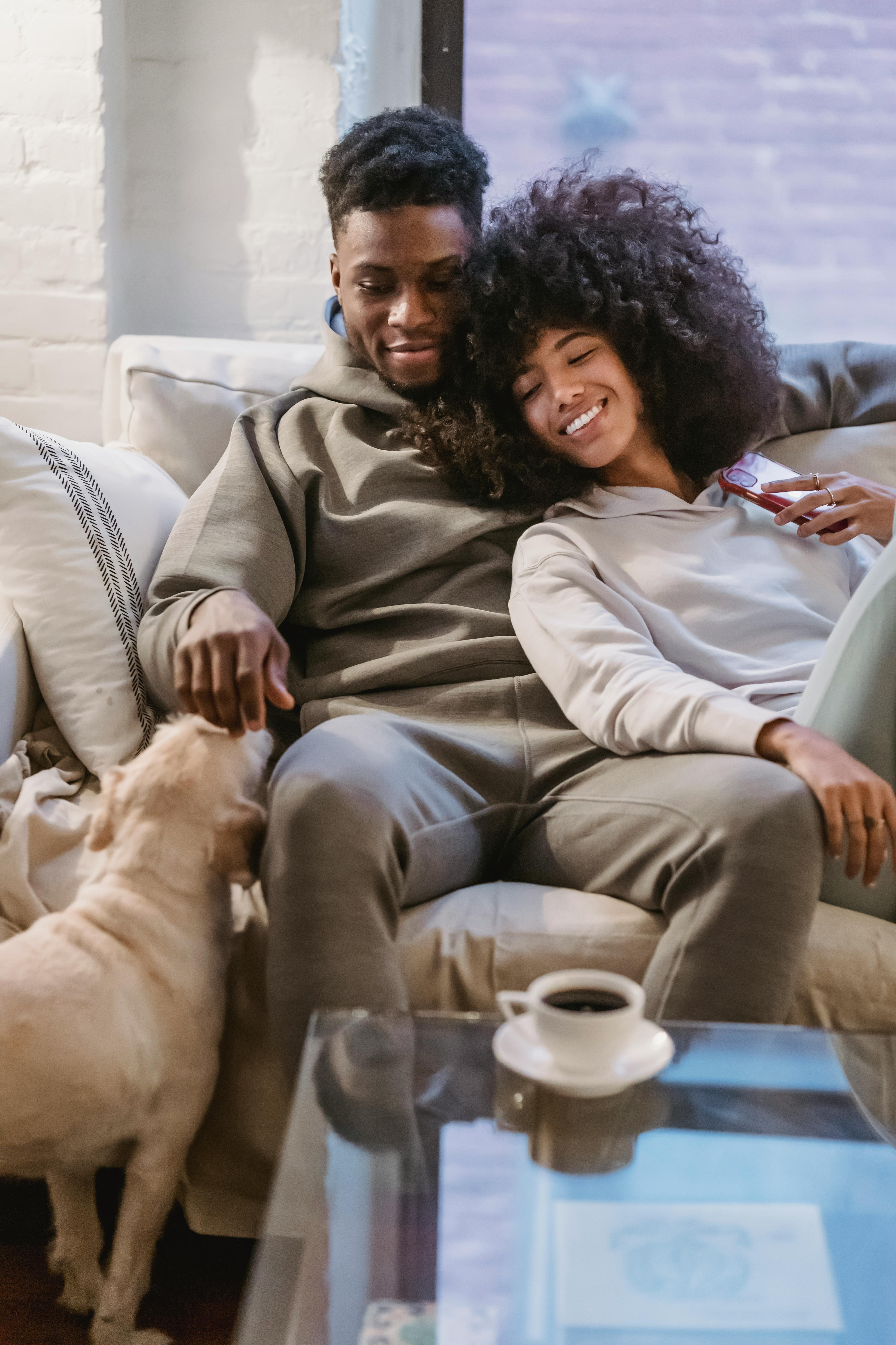 black couple cuddling on couch and petting dog 