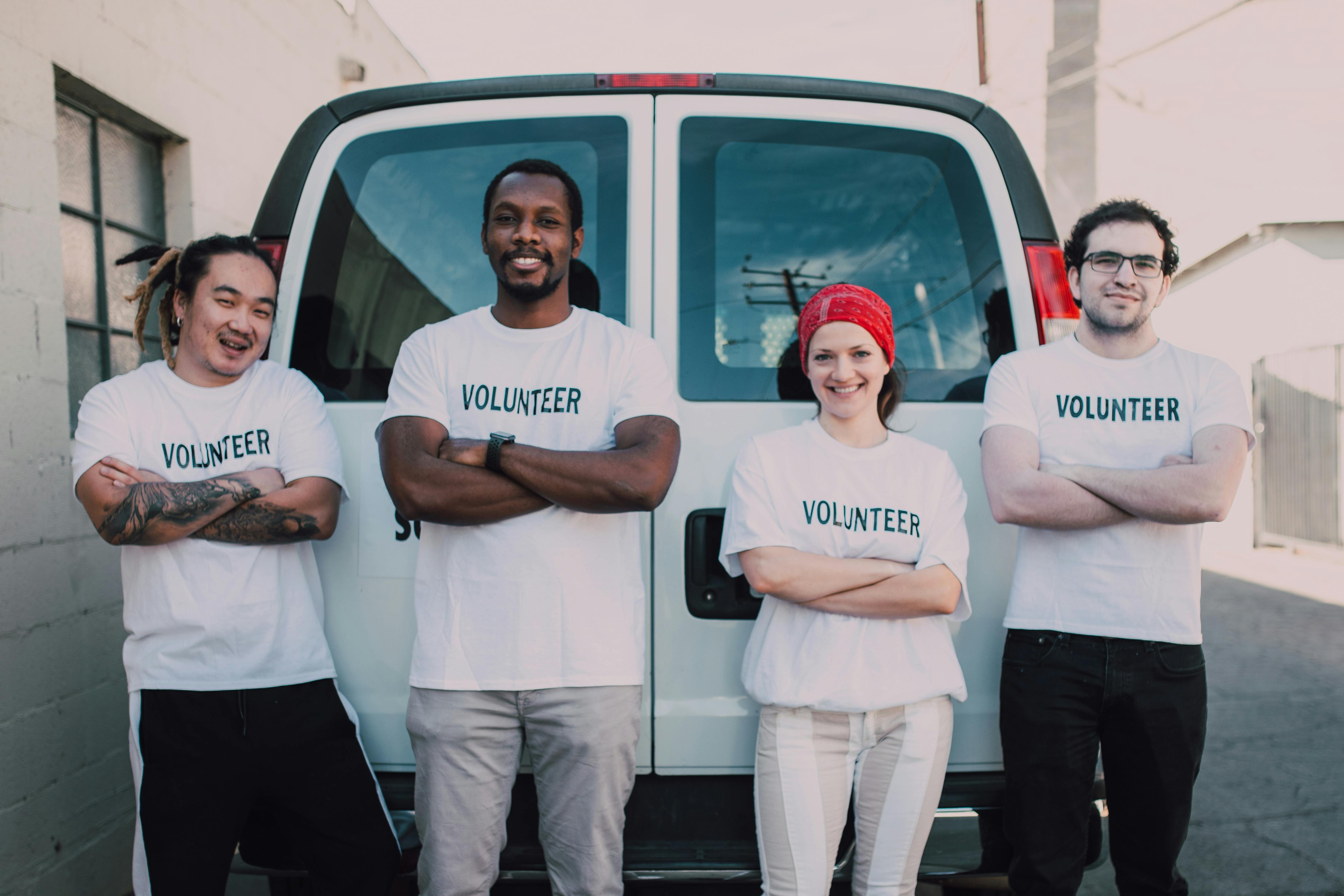 group of three men and one woman wearing white volunteer t-shirts standing behind a white van