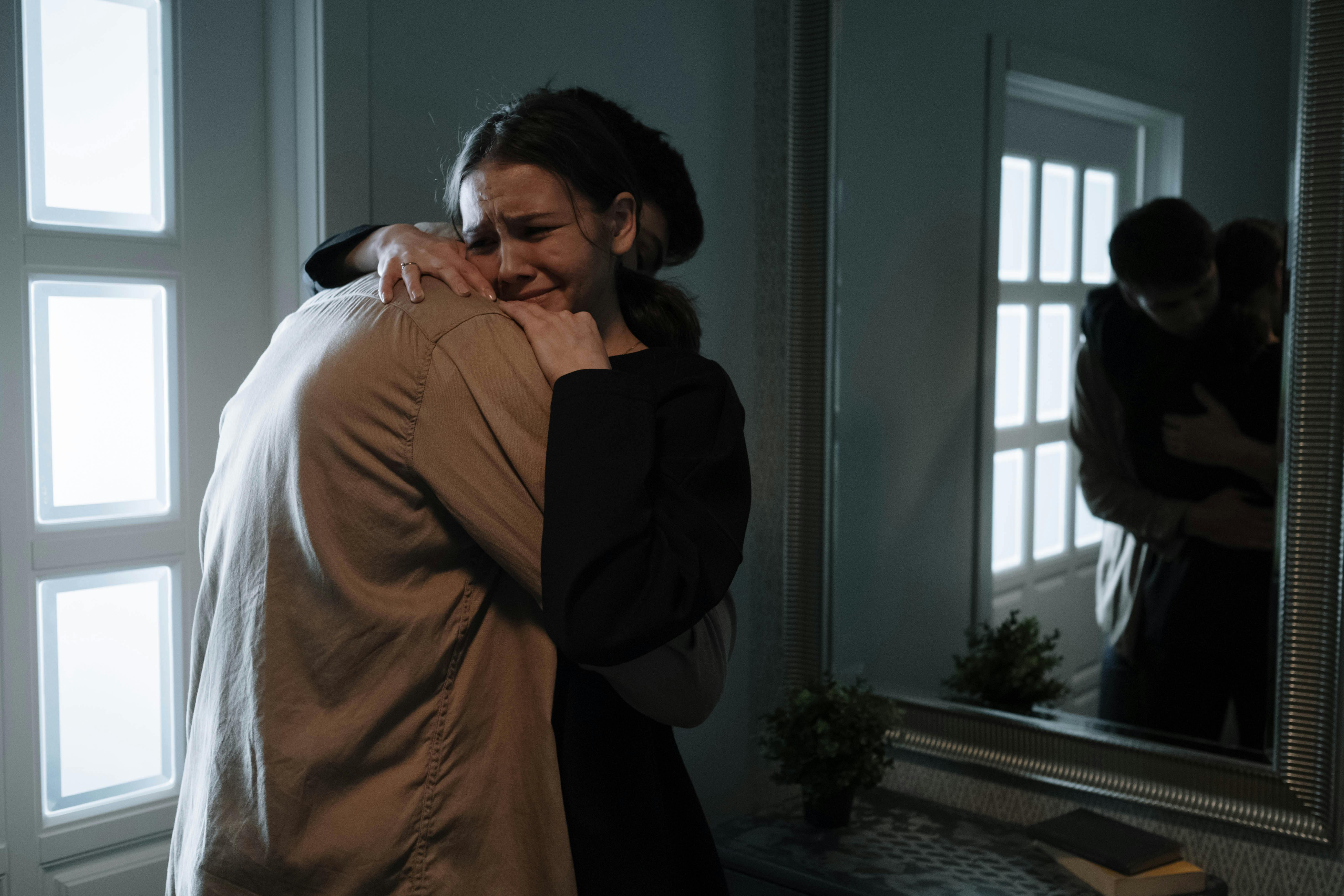 crying woman with brown hair and a black sweater hugging another person