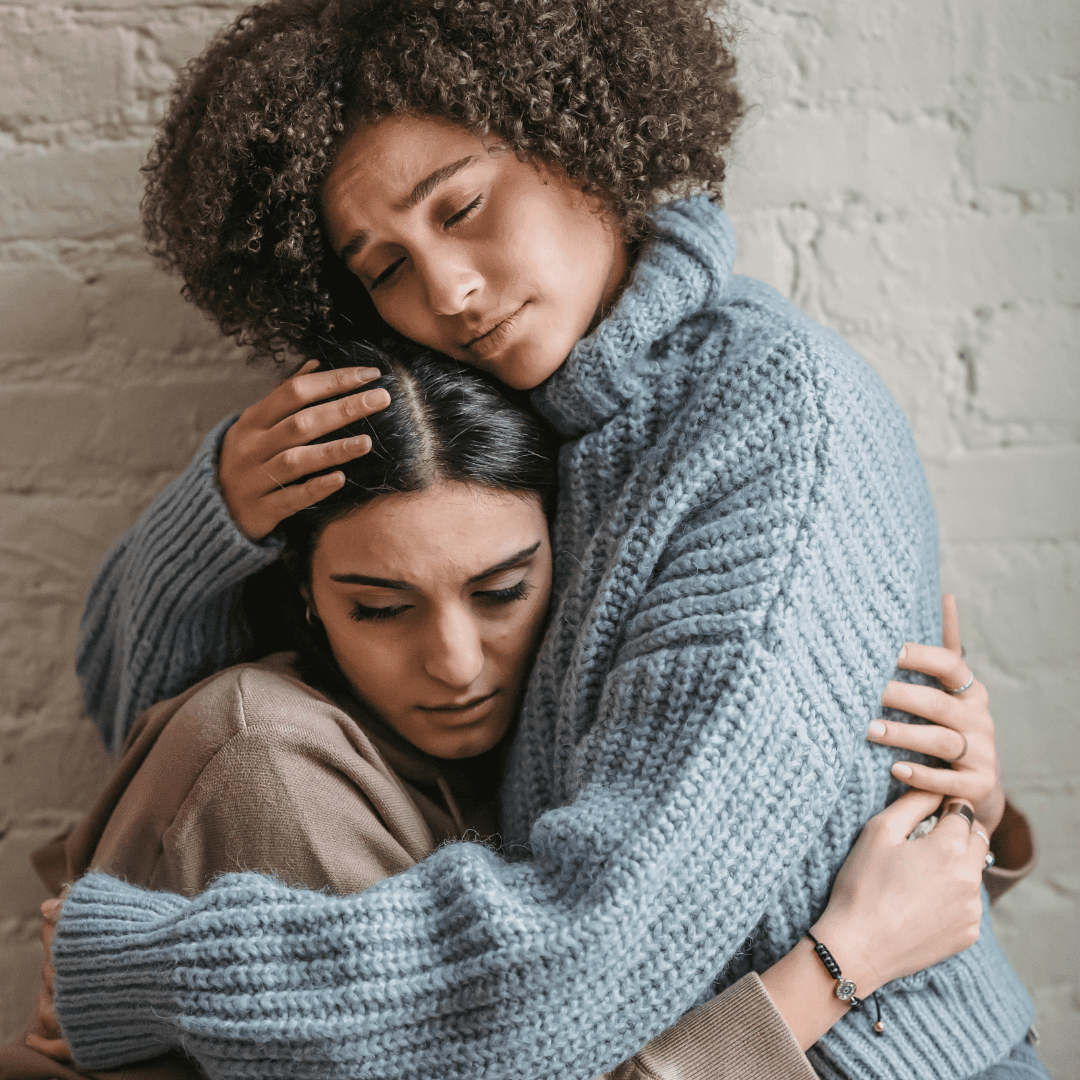 woman in grey sweater hugging woman in pink sweatshirt