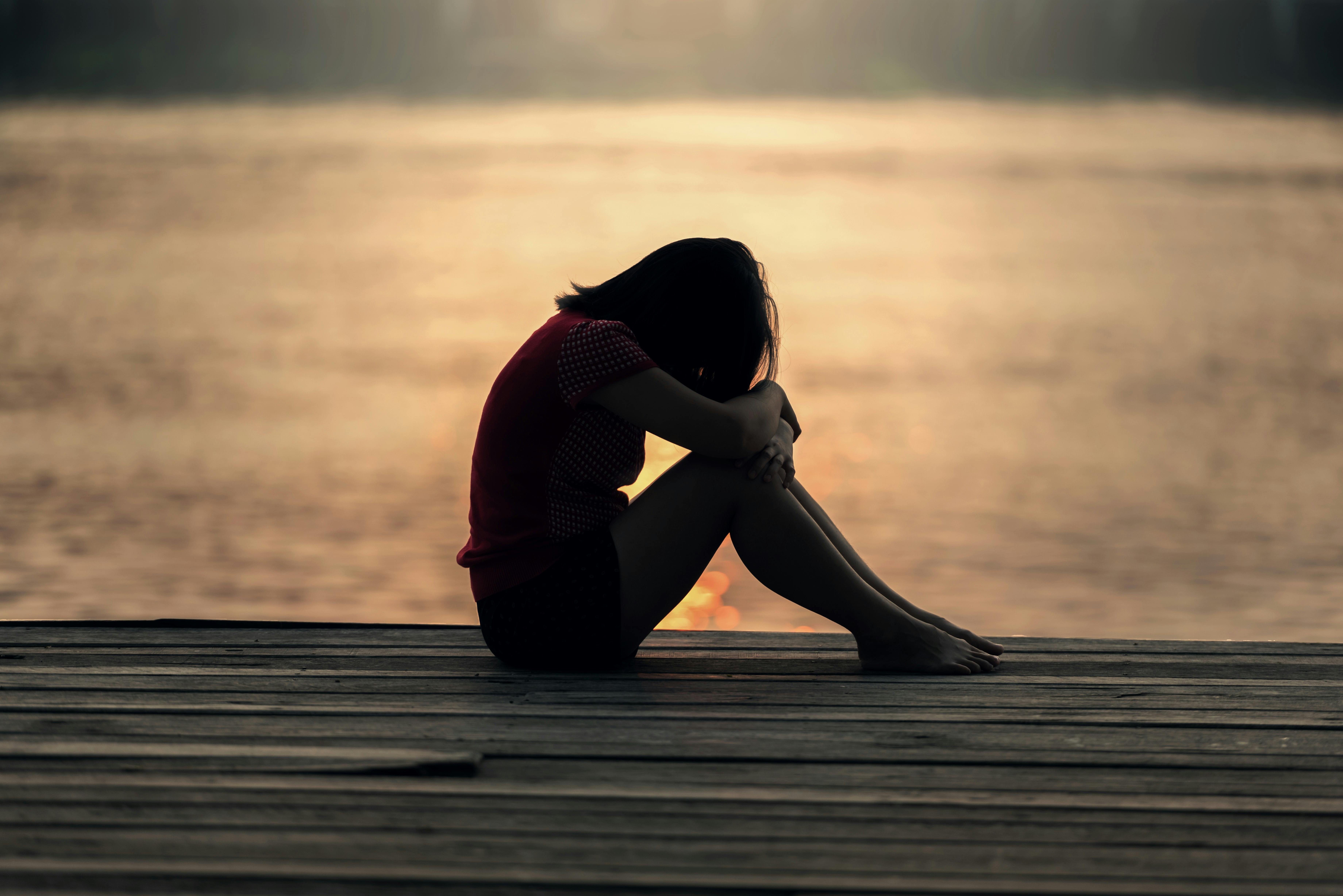 woman sitting on dock with head on knees at sunset