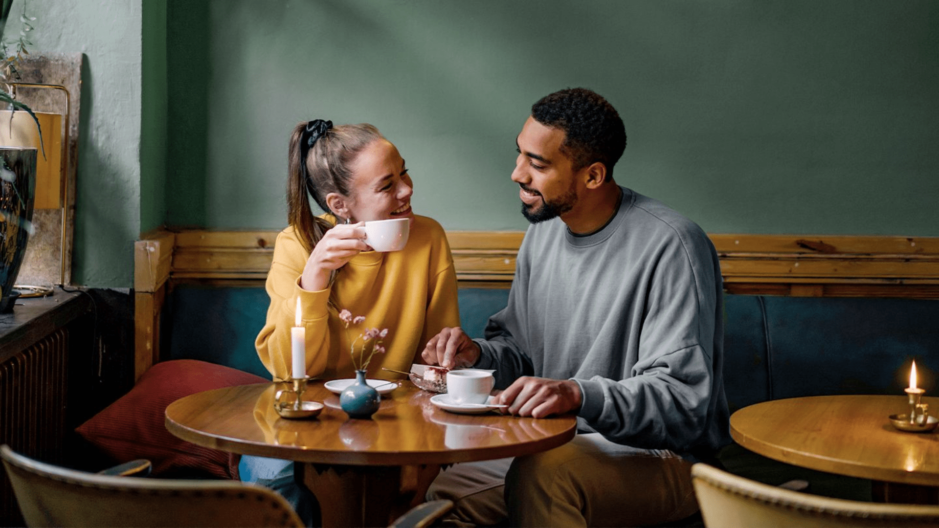 A smiling couple enjoying coffee and dessert at a cozy café, engaged in a warm conversation.