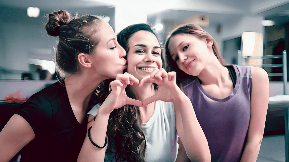 Three smiling friends posing together, forming a heart shape with their hands.