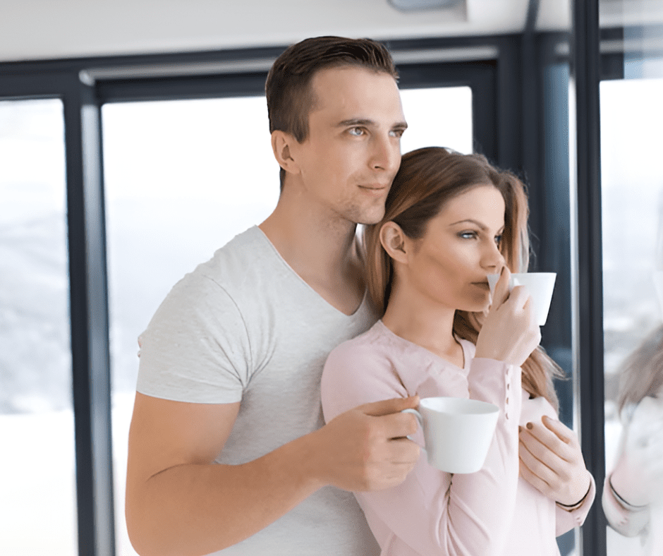 young-couple-drinking-coffee-by-window A young couple enjoying a quiet moment together while drinking coffee by a large window with a scenic view
