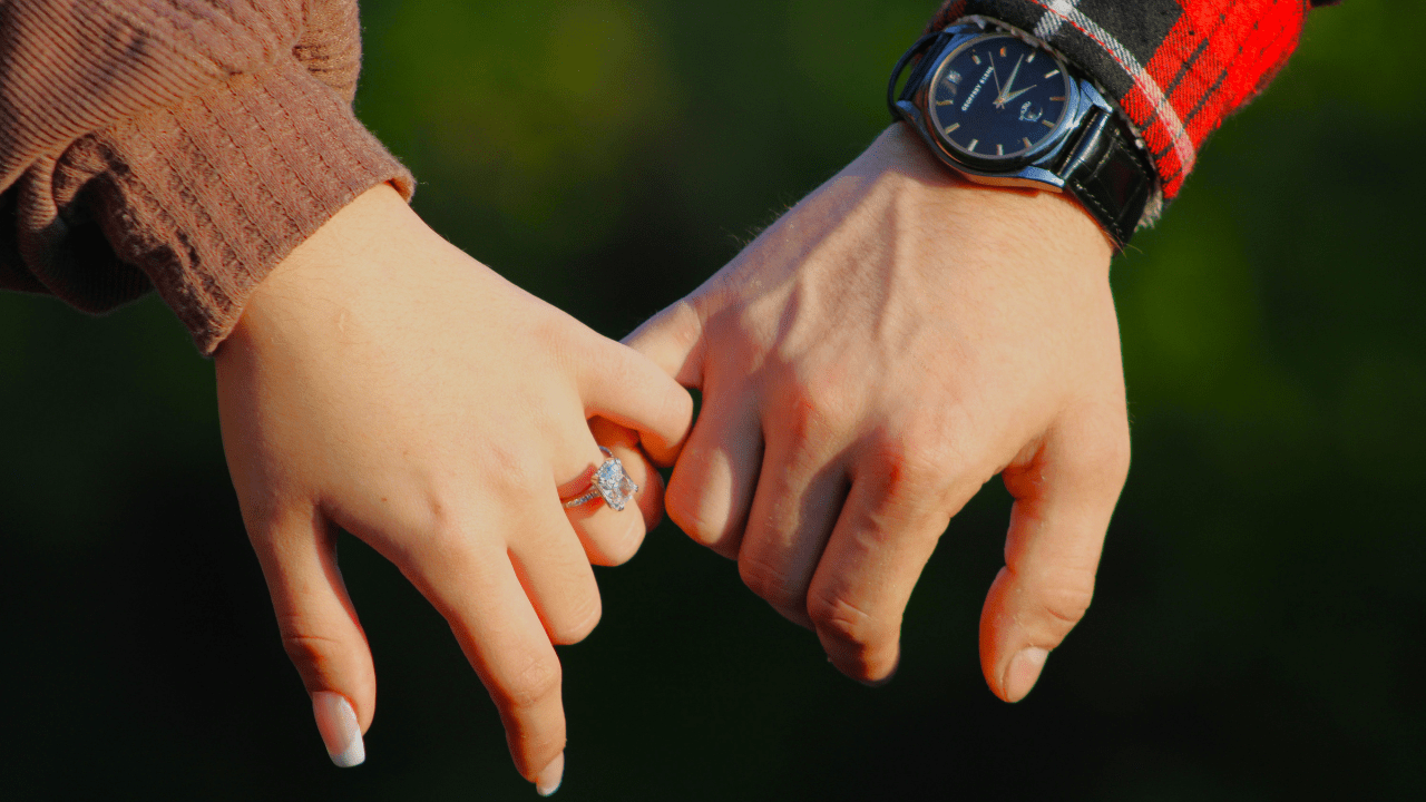 Close up of couple holding hands with engagement ring